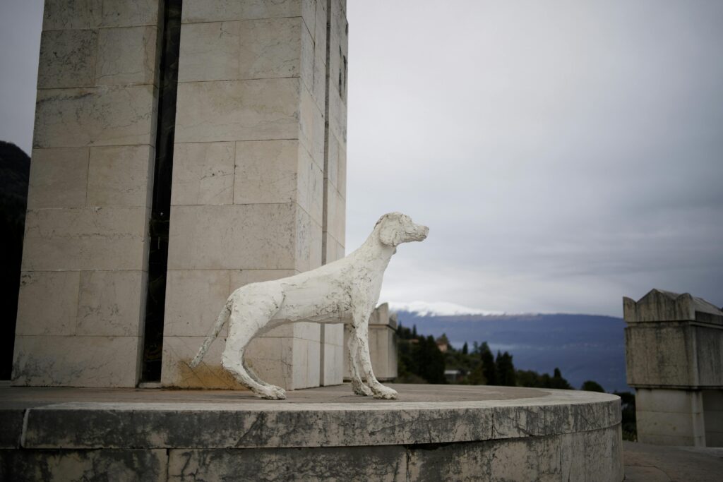 Statue of a dog at a monument in Gardone Riviera, Italy, with scenic views.